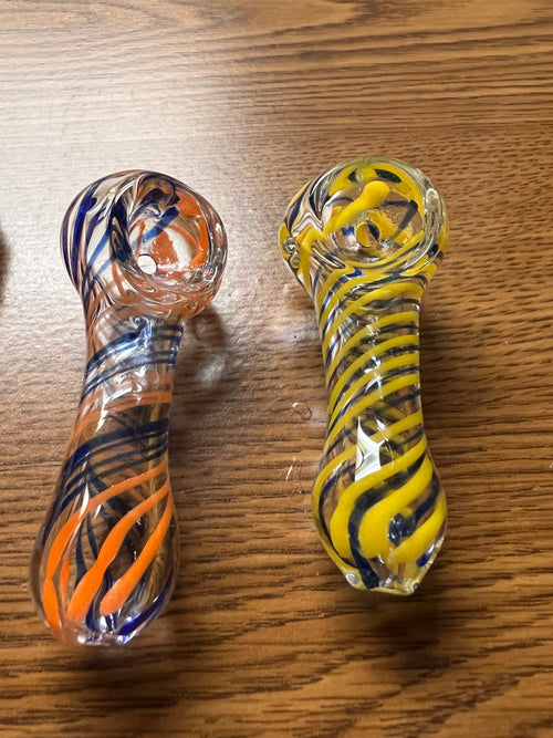 Two Ripkitty 3" striped swirly handblown glass spoon pipes side by side — orange and navy blue spiral stripe colorway (left) and yellow and navy blue spiral stripe colorway (right), shown on wood surface