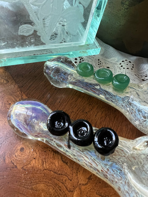 Close-up of two Ripkitty silver fumed frit glass hand pipes showing green jade and black rose marble accent details on textured frit bodies