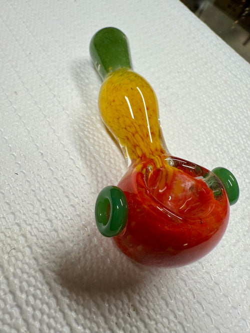 Side profile of Ripkitty rasta spoon pipe showing red bowl with green ring accents and yellow frit neck transitioning to green mouthpiece
